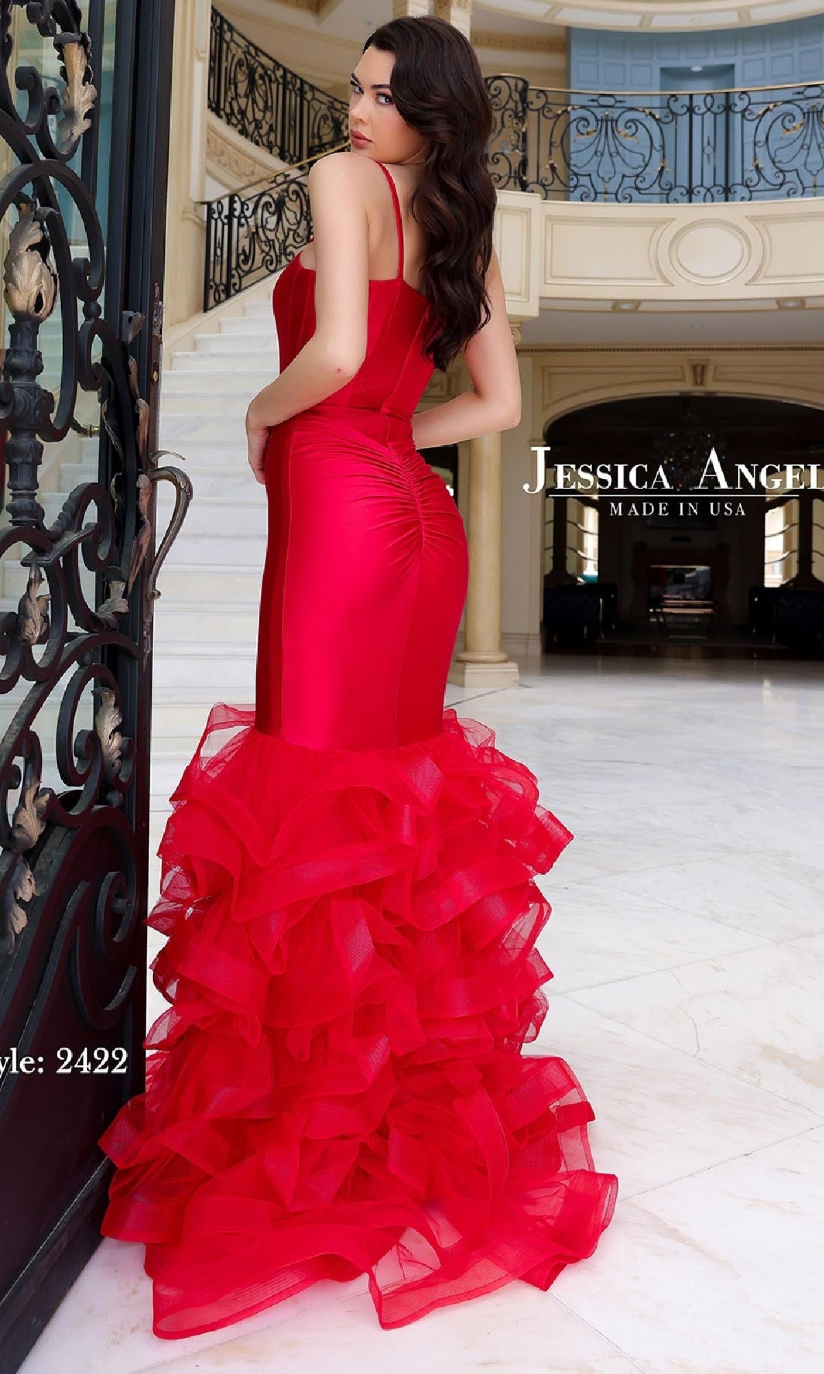 A woman stands in an elegant hall, wearing the Jessica Angel 2422 Long Ruffle Mermaid Prom Dress with a corset-style bodice and layered ruffled tulle hem.
